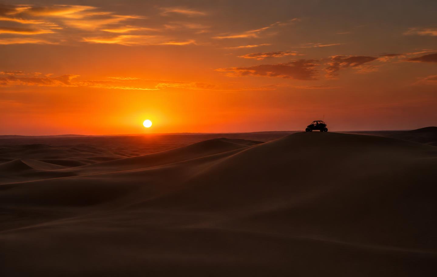 Pôr do sol sobre dunas com UTV na crista